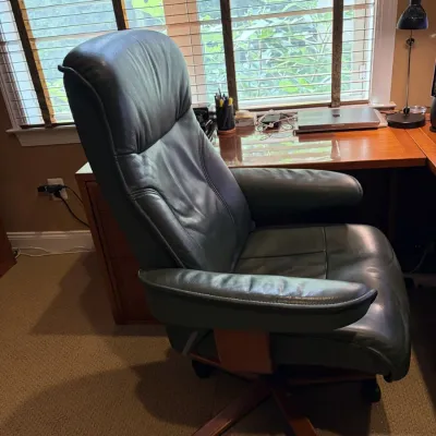 Ekornes Stressless high-back executive desk chair with dark green leather upholstery and a five-star wood base on casters.