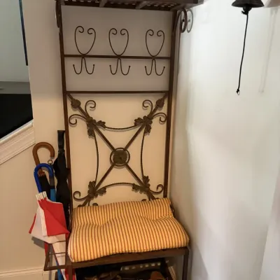 Wrought iron hall tree featuring scrollwork detailing, a top shelf, coat hooks, and a bench with a yellow striped cushion over a lower...