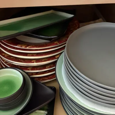 Collection of modern ceramic tableware including matte grey and mint green plates, small sauce dishes, rectangular platters, and a stack...