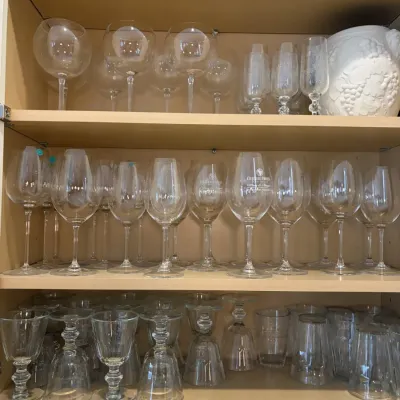 Collection of assorted glassware filling a light wood cabinet, featuring wine glasses, champagne flutes, goblet-style glasses, and tumblers.