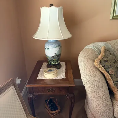 Hand-painted ceramic table lamp featuring a swan scene, paired with a classic wooden cabriole-leg end table.