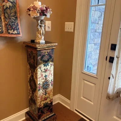 Ornate painted pedestal stand featuring intricate floral scrollwork panels, topped with a cherub candleholder.