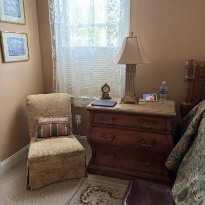 Traditional bedroom corner featuring a serpentine-front three-drawer nightstand with marble top, a classic column table lamp, and an...