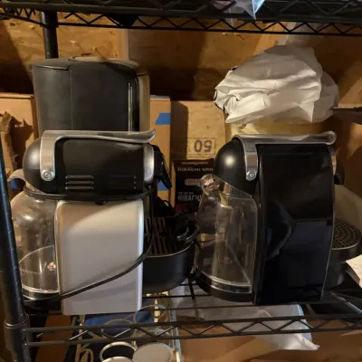 Pair of black and silver Nespresso espresso machines stored on a wire shelving rack.