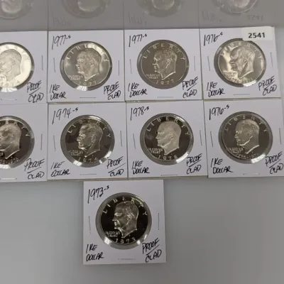 Collection of nine Eisenhower clad proof silver dollars dating from 1973 to 1978, individually housed in cardboard coin flips.