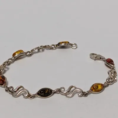Sterling silver chain bracelet featuring marquise-cut amber stones in varied honey, cognac, and green hues, connected by scrollwork links.
