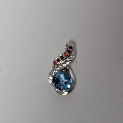 Sterling silver scroll pendant featuring a round faceted London blue topaz accent, small pave diamonds, and dark red gemstone accents.