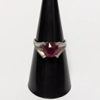 Vintage silver-tone ring featuring a round, brilliant-cut red glass or synthetic ruby gemstone in a four-prong setting.