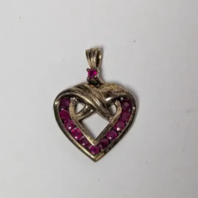 Sterling silver heart-shaped pendant featuring an intertwined ribbon design accented with round synthetic ruby stones.