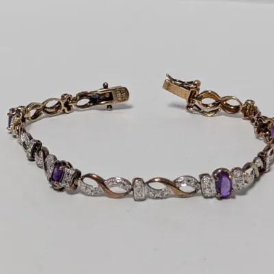 Gold tennis-style bracelet featuring oval-cut purple gemstone accents alternating with diamond-set twist links and a box clasp with...