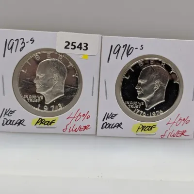 Two Eisenhower silver proof dollars, featuring a 1973-S and a 1976-S Bicentennial issue, each housed in cardboard coin flips.