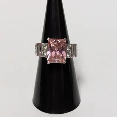 Sterling silver ring featuring a large radiant-cut pink stone flanked by clear cubic zirconia and baguette-cut accent stones, displayed...