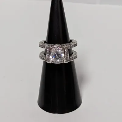 Silver-tone bridal set featuring a round solitaire stone flanked by paved guard bands, displayed on a black ring cone.