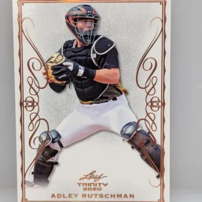 2020 Leaf Trinity Adley Rutschman baseball trading card featuring ornate bronze foil scrollwork bordering the catcher.