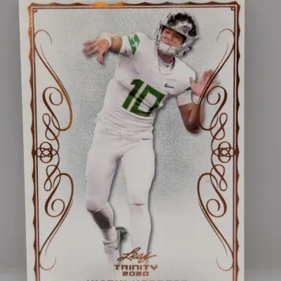 2020 Leaf Trinity Justin Herbert rookie trading card featuring an ornate metallic copper border and the quarterback in his Oregon Ducks...