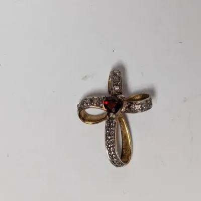 Gold-tone ribbon cross pendant featuring clear pave accents and a heart-cut red stone center.