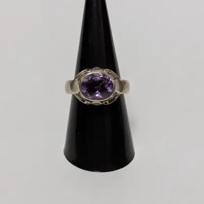 Sterling silver solitaire ring featuring an oval faceted purple amethyst gemstone, displayed on a black ring cone.