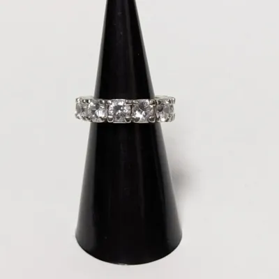 Sterling silver or white gold eternity band set with round cut cubic zirconia or diamonds, displayed on a black ring cone.