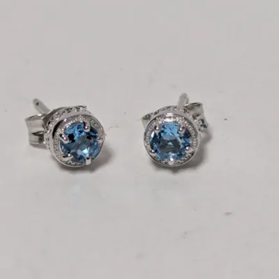 Pair of round-cut blue topaz stud earrings in a white metal setting with milgrain detailing and post backs.