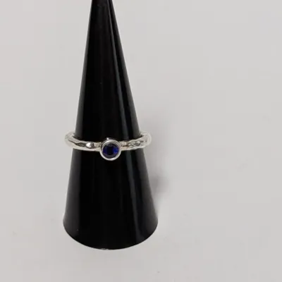 Sterling silver solitaire ring featuring a bezel-set blue stone on a textured band, displayed on a black ring cone.