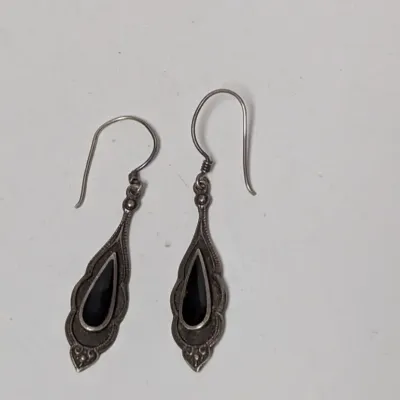 Pair of sterling silver dangle earrings featuring teardrop-shaped black onyx stones in an ornate vintage setting with french wire hooks.