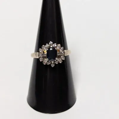 Vintage sterling silver ring featuring a dark oval blue sapphire surrounded by a halo of clear accent stones, displayed on a black ring...