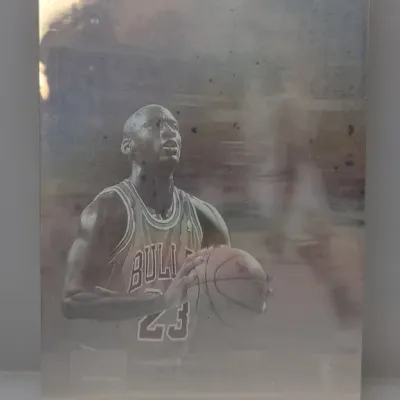 Metallic print or trading card featuring Michael Jordan in his Chicago Bulls jersey, showing light surface wear and smudging.