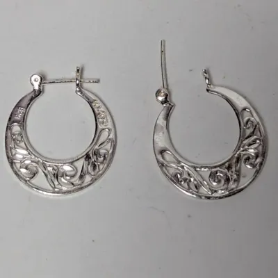 Pair of sterling silver crescent hoop earrings featuring intricate scrollwork filigree detailing and latch-back closures.