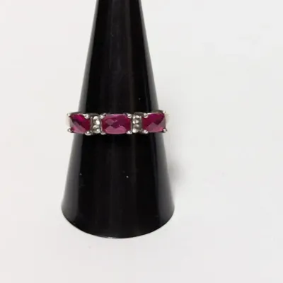 Sterling silver ring featuring three cushion-cut magenta gemstones separated by small clear accent stones, displayed on a black ring cone.