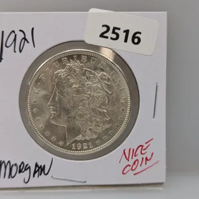 1921 Morgan silver dollar housed in a protective cardboard flip holder with handwritten notes.