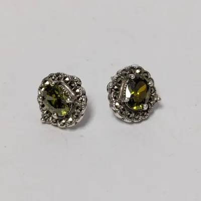 Pair of sterling silver stud earrings featuring oval olive green faceted gemstones encircled by marcasite halos.