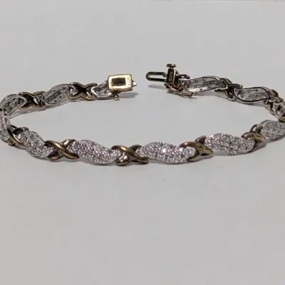 Two-tone silver and gold-tone tennis bracelet featuring alternating pave-set clear stones and 'X' shaped links with a box clasp...
