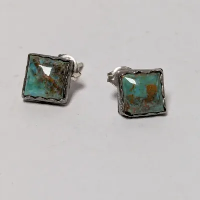Pair of Southwest style sterling silver and turquoise stud earrings featuring square cabochons with natural matrix and notched bezel frames.