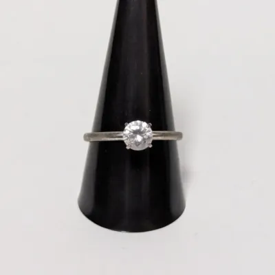 Classic solitaire ring featuring a round-cut clear stone set in a simple metallic band, displayed on a black ring cone.