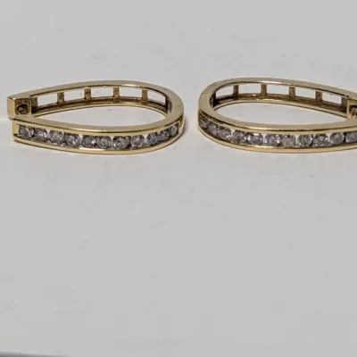 Pair of yellow gold oval hinged hoop earrings featuring channel-set round clear stones.