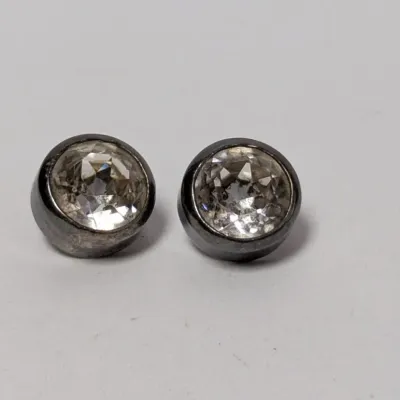 Pair of bezel-set clear stone stud earrings featuring round-cut crystals or glass in dark metal settings.