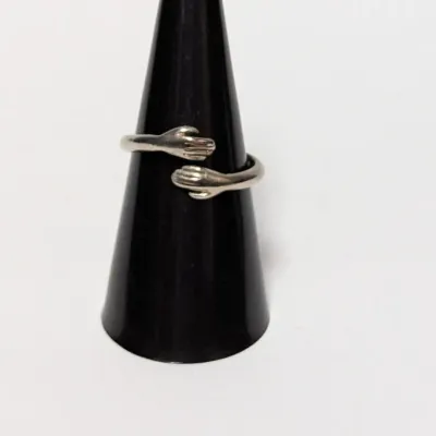 Silver-tone metal hugging hands ring displayed on a black ring cone.