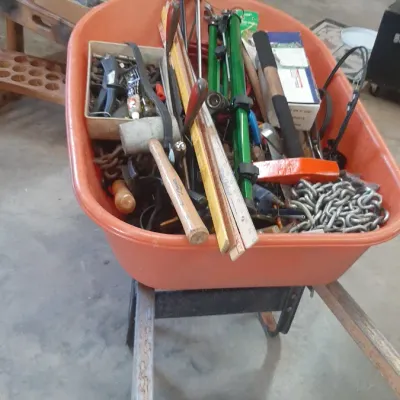 Orange wheelbarrow filled with assorted hand tools, chains, wooden levels, and hardware.
