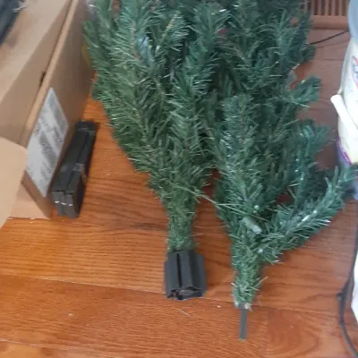 Disassembled artificial Christmas tree sections with green faux pine needles lying on a hardwood floor.