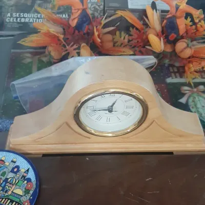 Light wood mantel clock with a brass bezel and Roman numeral dial, displayed alongside autumn decor and a decorative plate.