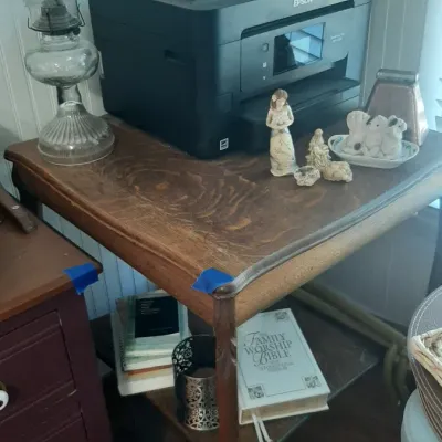 Black Epson all-in-one printer sitting on a vintage wooden side table alongside a clear glass oil lamp and small decorative figurines.