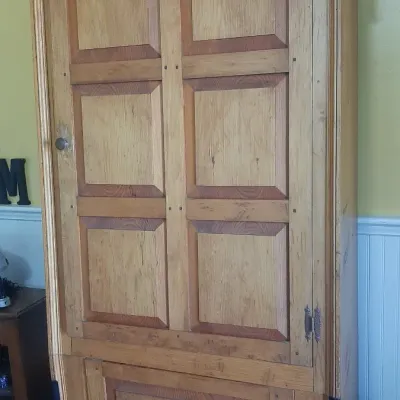 Rustic pine wooden armoire or storage cabinet featuring panel doors, brass hardware, and a natural finish.