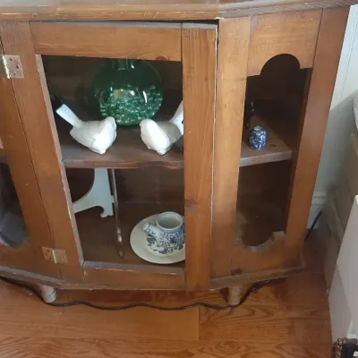 Vintage wooden corner display cabinet with glass door panels, housing decorative ceramic bird figurines and glassware.