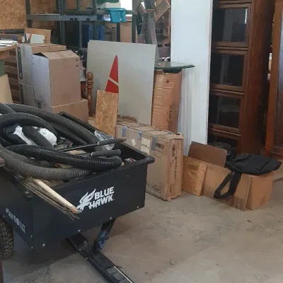 Black Blue Hawk dump cart filled with shop hoses, alongside a stackable glass-front wooden bookcase and assorted storage items in a...