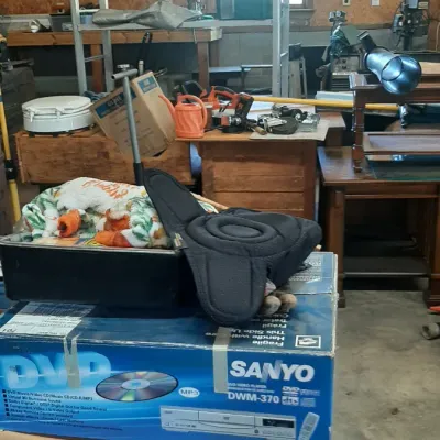 A stack of boxed goods including a Sanyo DVD player in its original box and a Summit Racing Equipment shipping box, set inside a workshop.