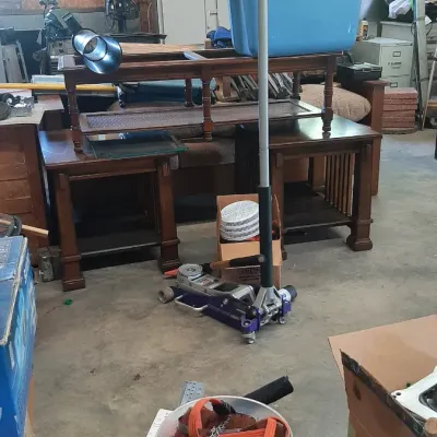 A workshop interior featuring a hydraulic floor jack, wooden end tables, a coffee table, and various tools and storage containers.