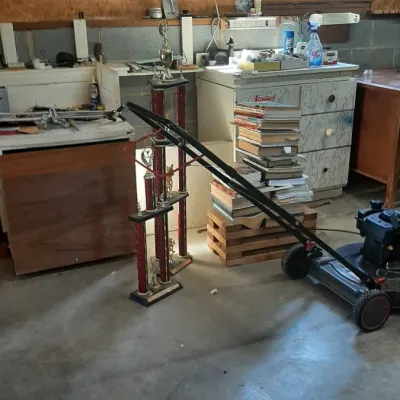 Workshop and garage area featuring a push lawn mower, large multi-tier sports trophies, a stack of books, and various storage cabinets.