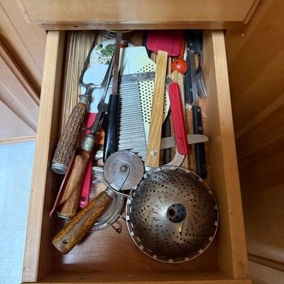 Sale Photo Thumbnail #42: Assorted vintage kitchen utensils contained inside a wooden drawer, including stag-handle carving forks, a pizza cutter, and a folding steamer basket.