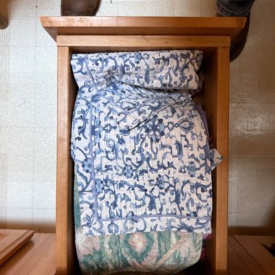 Sale Photo Thumbnail #47: Wooden furniture drawer filled with folded textiles, including a blue and white floral quilted item and a pastel pattern quilt.