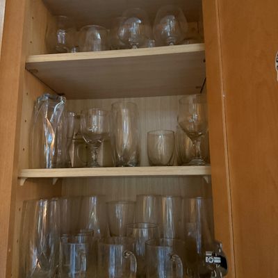 Sale Photo Thumbnail #34: Collection of assorted glassware, including stemware, glass mugs, and highball glasses, arranged inside a wooden cabinet.